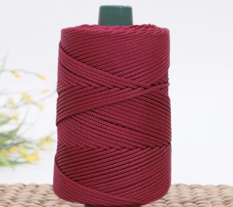 A spool of deep red crochet ice rope with a dark green cap resting on a woven mat.