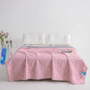 A pink cooling summer blanket is laid out on a bed with white pillows and a light blue accent.