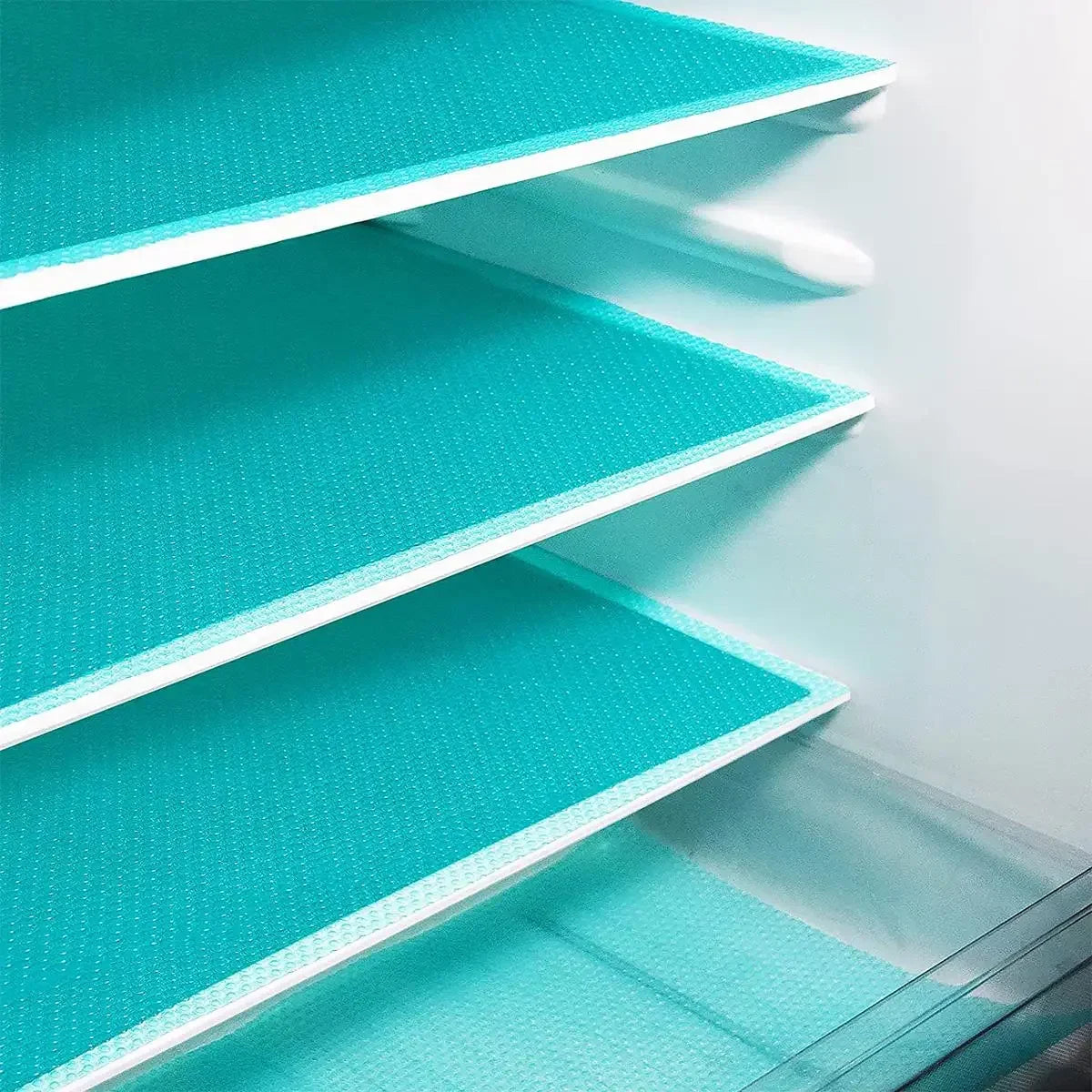 A close-up view of multiple teal reusable EVA fridge shelf liners stacked in a white organizer.