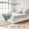 White bed with a ruffled skirt and bedding set on a wooden floor.