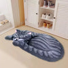 A gray cartoon cat plush rug lying on a light floor next to a white cabinet with shoes.