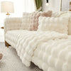 A white plush cushion cover draped over a sofa with light beige accents and a nearby lamp.