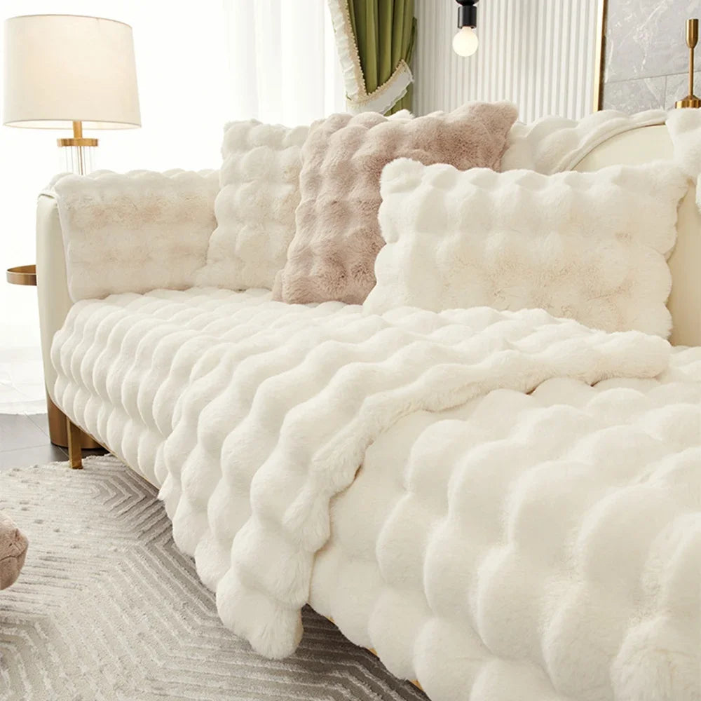 A white plush cushion cover draped over a sofa with light beige accents and a nearby lamp.