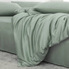 A draped sage green luxury bamboo duvet cover set on a bed with a gray carpet.
