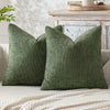 A close-up of a moss green chenille pillow cover with a textured weave resting on a light-colored sofa.