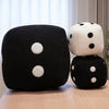 A pair of black and white polka-dotted dice plush throw pillows resting on a light wooden surface.
