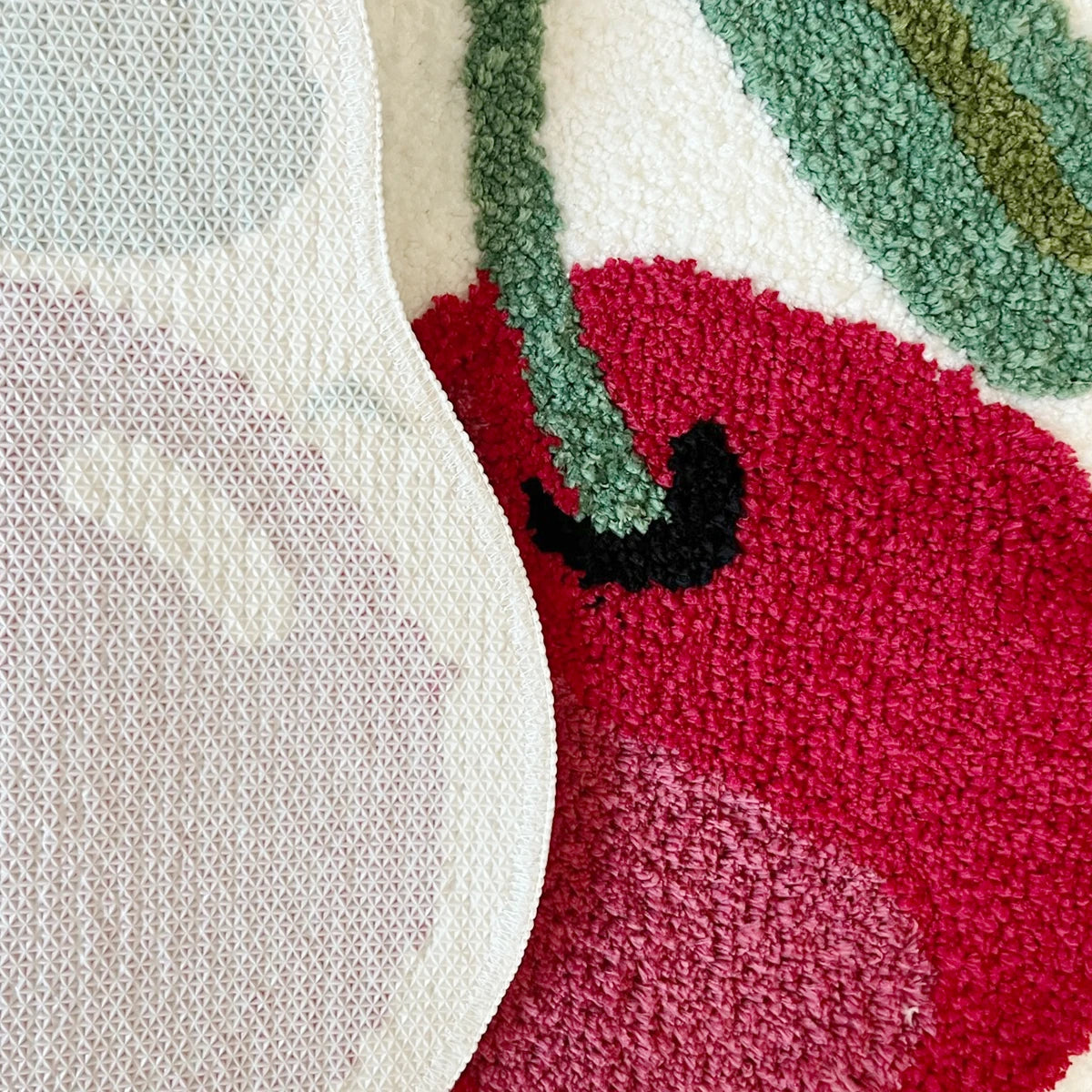 Blush pink soft tufted area rug with an organic shape featuring shades of green and red.