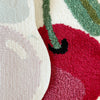 Blush pink soft tufted area rug with an organic shape featuring shades of green and red.