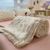 A rolled light cream quilt blanket with a floral print is displayed on a pink surface.