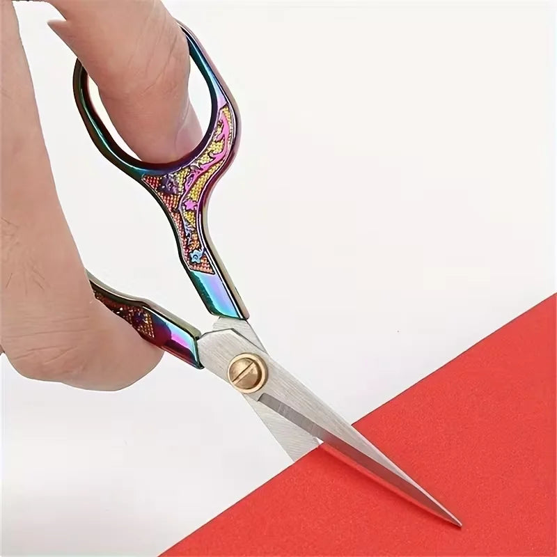 A pair of vintage stainless steel sewing scissors with colorful handles rests on a red surface.