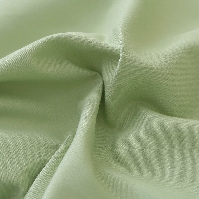 A close-up of a smooth, pale sage green polyester fabric pillow cover set.