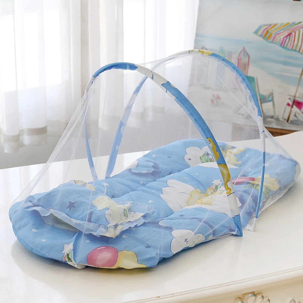 A portable baby crib net with soft blue and white padding is displayed on a white surface.