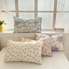 A collection of floral printed pillow covers in shades of blue, purple, and cream displayed on a white surface near a window.
