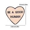A light pink heart shaped embroidery patch with the text BE A GOOD HUMAN embroidered in dark gray thread.