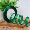 Roll of green satin ribbon with white filling on a wooden surface