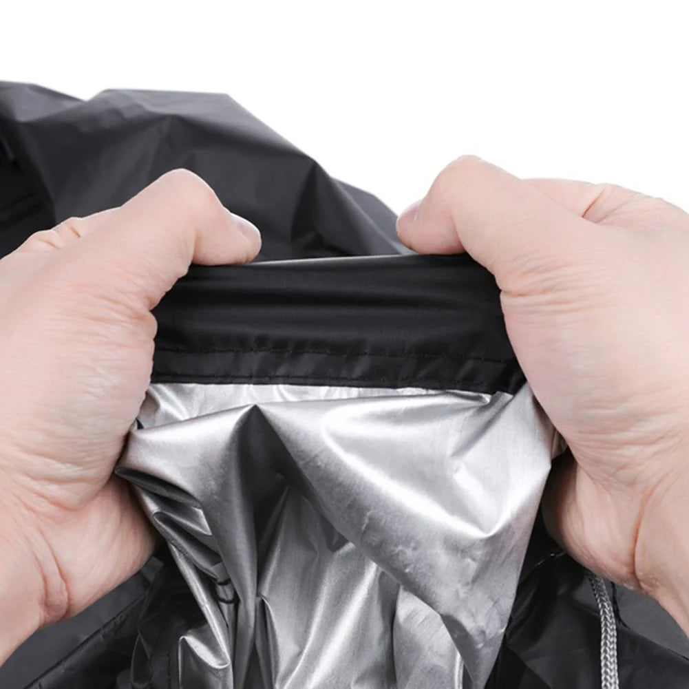 Hands holding a black waterproof BBQ grill cover open to reveal a shiny silver lining.