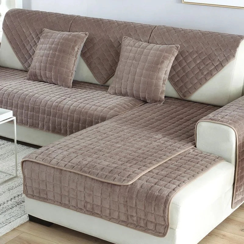 A beige quilted sofa protection cover with matching pillows on a white leather sofa.