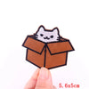A brown cardboard box shaped like a cat is embroidered with a white cartoon cat face on a fabric patch.