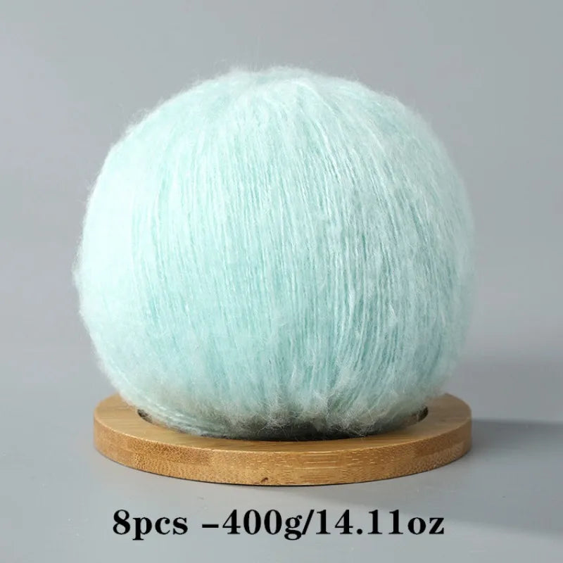 A ball of light mint green mohair yarn resting on a wooden base.