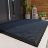 A dark blue non-slip rubber doormat with a diamond pattern placed on a light gray floor.