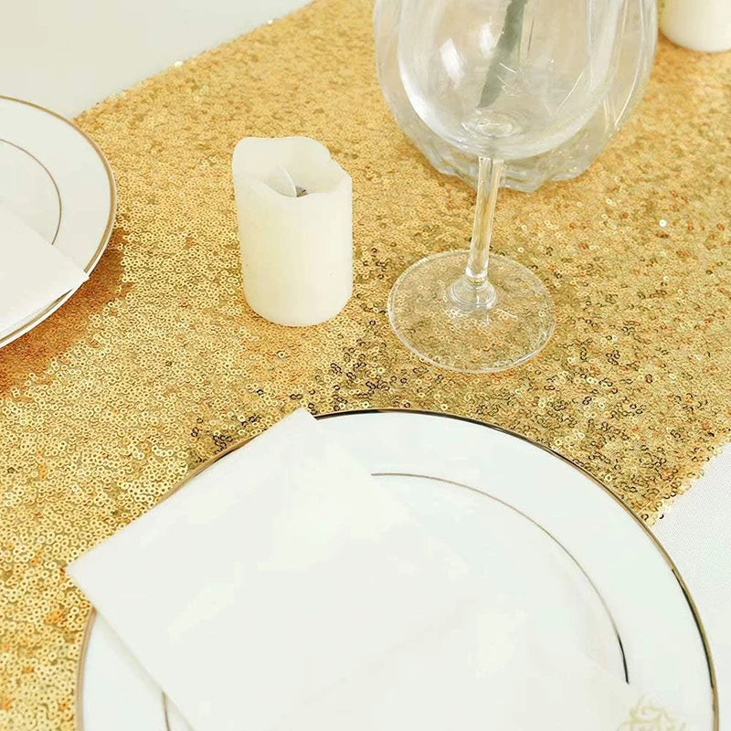 Golden sequin table runner with a white candle and a glass of wine on a gold textured surface.