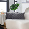 Two gray quilted velvet decorative pillow covers on a white sofa with a large green monstera leaf in the background