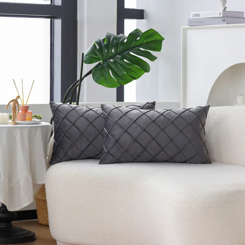 Two gray quilted velvet decorative pillow covers on a white sofa with a large green monstera leaf in the background