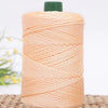A spool of light peach colored crochet ice rope with a green cap, resting on a woven mat.