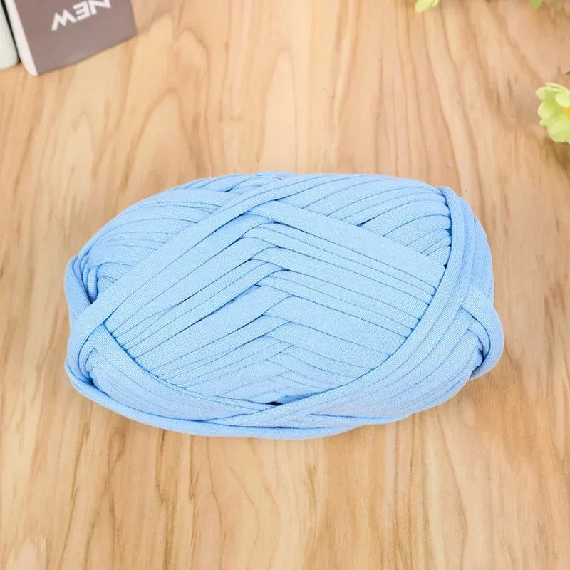 A ball of light blue flat thread yarn for crafting and sewing lying on a wooden surface.