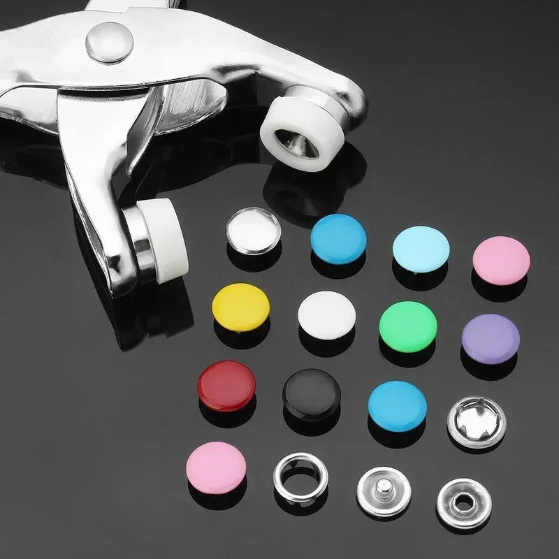 A collection of colorful metal sewing buttons and a silver tool are displayed on a dark surface.