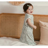 A smiling baby wearing a light green patterned soft cotton sleeping bag or swaddle, lying on a white surface.