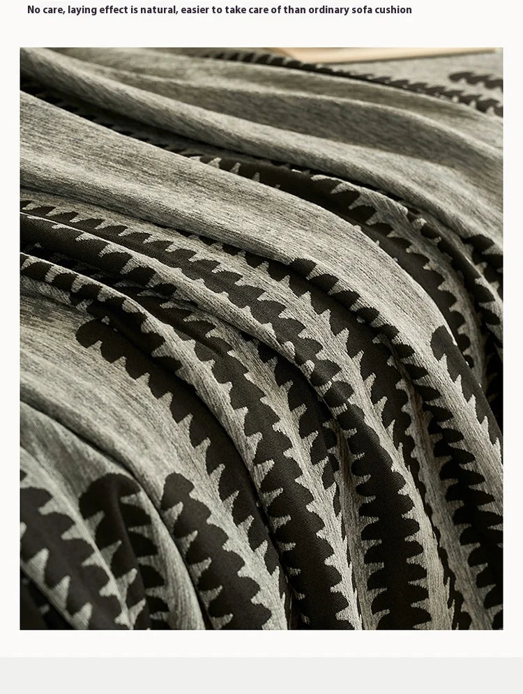 Close-up of a gray and black herringbone chenille sofa cover with decorative tassel fringes.