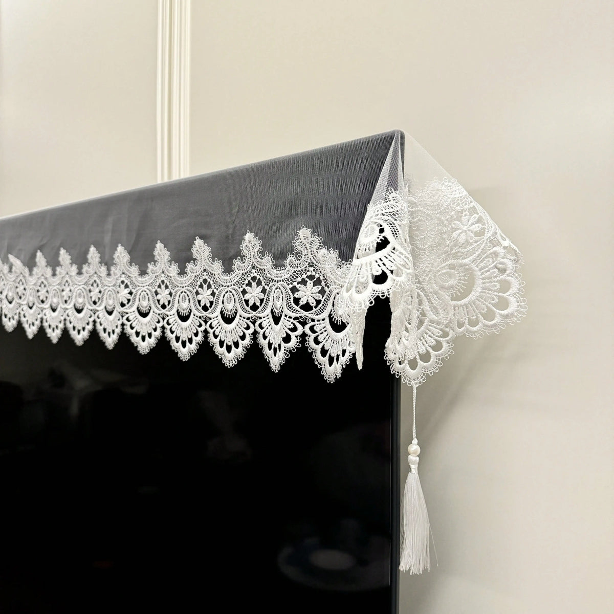 Black table runner with white embroidered mesh lace trim and tassels hanging on a wall.