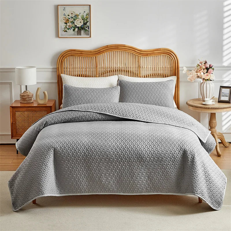 A gray quilted duvet and pillow set displayed on a wooden bed frame in a bright bedroom setting.