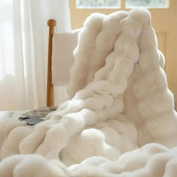 A fluffy white faux rabbit fleece throw blanket draped on a surface near a window.