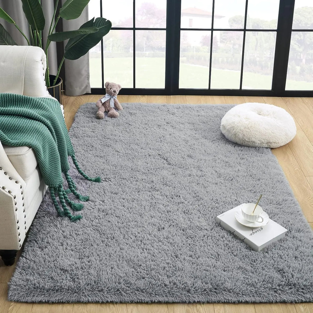 A gray tie-dyed plush floor mat with a white ceramic cup and spoon on it, placed in a bright room.