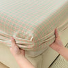 Hands are holding up a light green and pink plaid pure cotton fitted sheet.