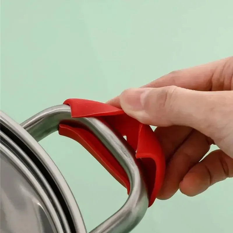 A hand is placing a red silicone pan handle cover onto a silver pot handle.