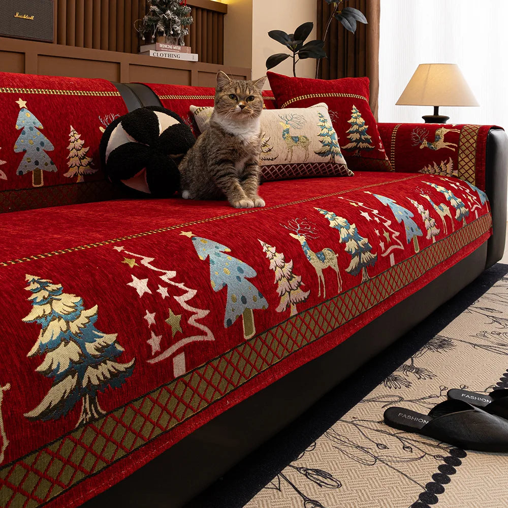 A red sofa mat cover featuring a Christmas deer pattern and forest motifs, with a tabby cat sitting on the fabric.