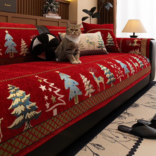 A red sofa mat cover featuring a Christmas deer pattern and forest motifs, with a tabby cat sitting on the fabric.