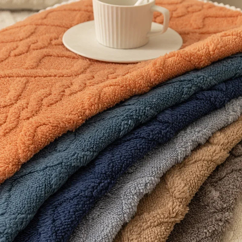 A stack of plush winter sofa cushion covers in various shades of orange, blue, and gray with a white cup on top