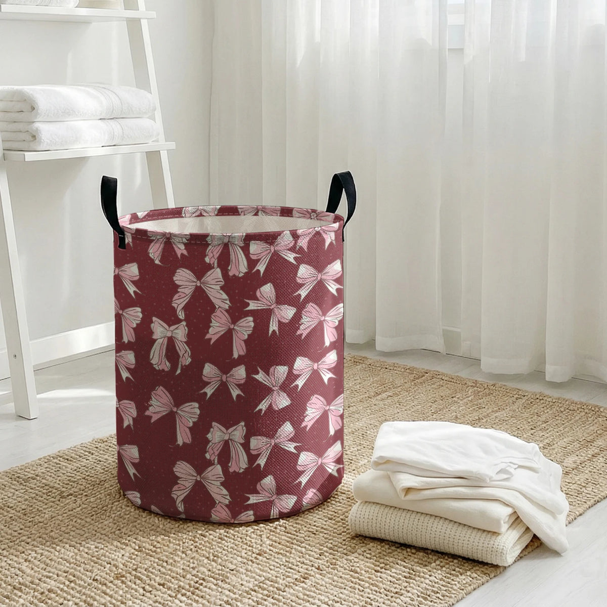 A round, maroon canvas laundry basket with a white bow pattern sits on a woven rug next to sheer white curtains.