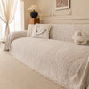 A beige herringbone chenille sofa cover with white accent pillows and a decorative lamp on a wooden stand.