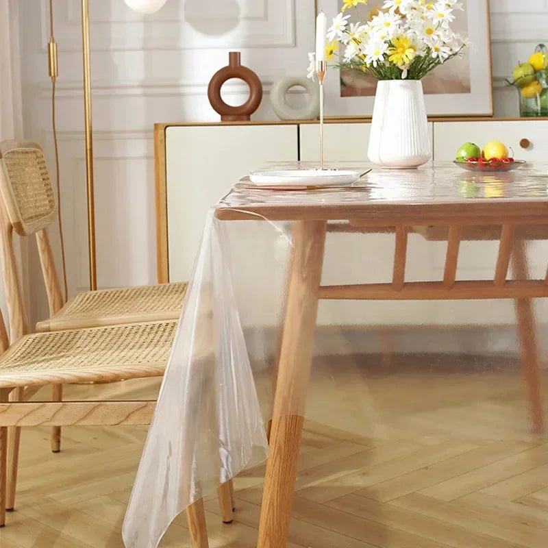 A clear heat-resistant PVC tablecloth protector draped over a wooden dining table in a bright room.