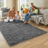 A family of three is playing on a gray tie-dyed plush floor mat in a living room.