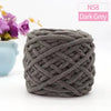 Dark grey chunky velvet knitting yarn in a skein, displayed next to purple flowers.