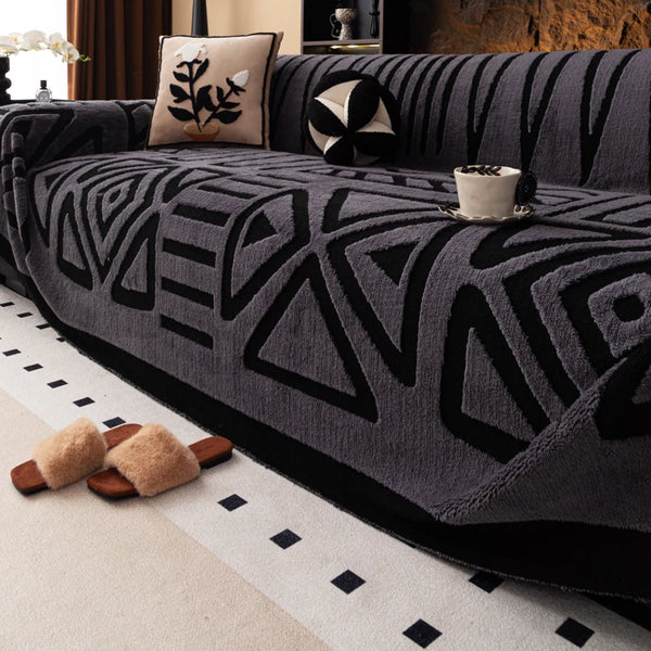 A dark gray knit sofa protector featuring a geometric pattern on a sofa, with tan slippers resting on the floor.
