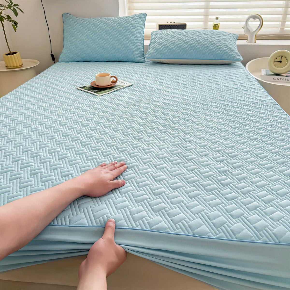 A light blue cooling spandex fitted sheet mattress protector is shown on a bed, with a hand touching the fabric.