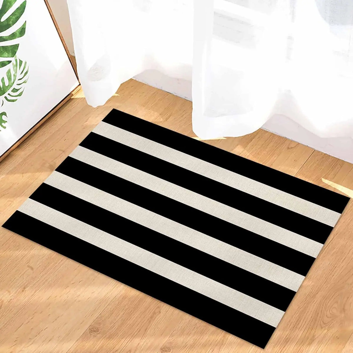 A black and white striped anti-slip door mat lying on a wooden floor next to a bright window.