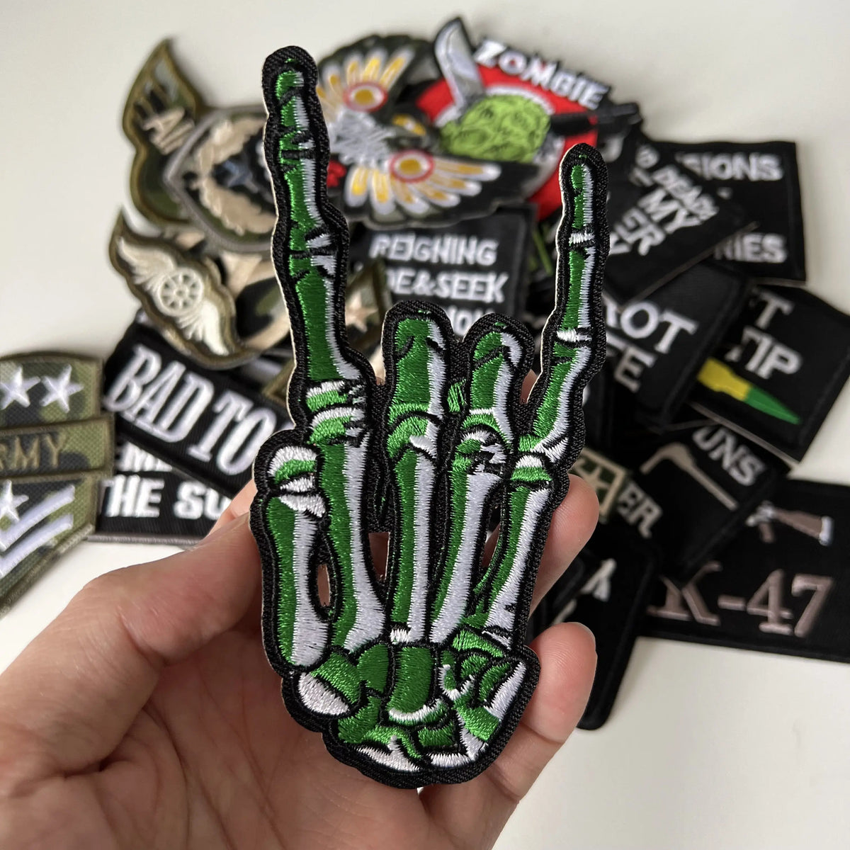 A hand holds a green and white iron-on slogan patch featuring a stylized handprint against a background of various black patc